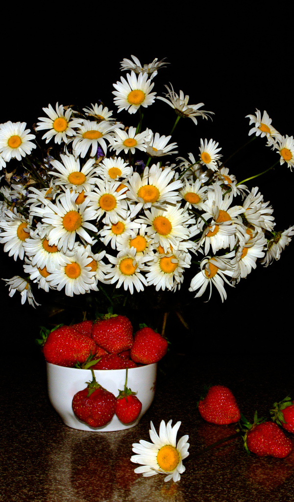 Белые полевые ромашки и клубника на столе на черном фоне