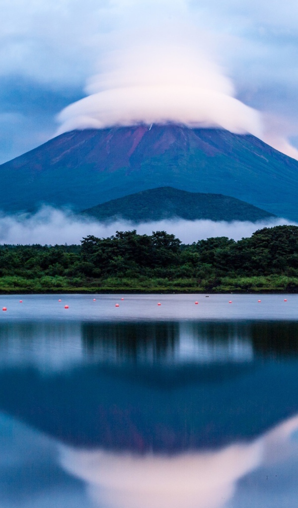 Вулкан Фудзияма в белых облаках отражается в воде озера