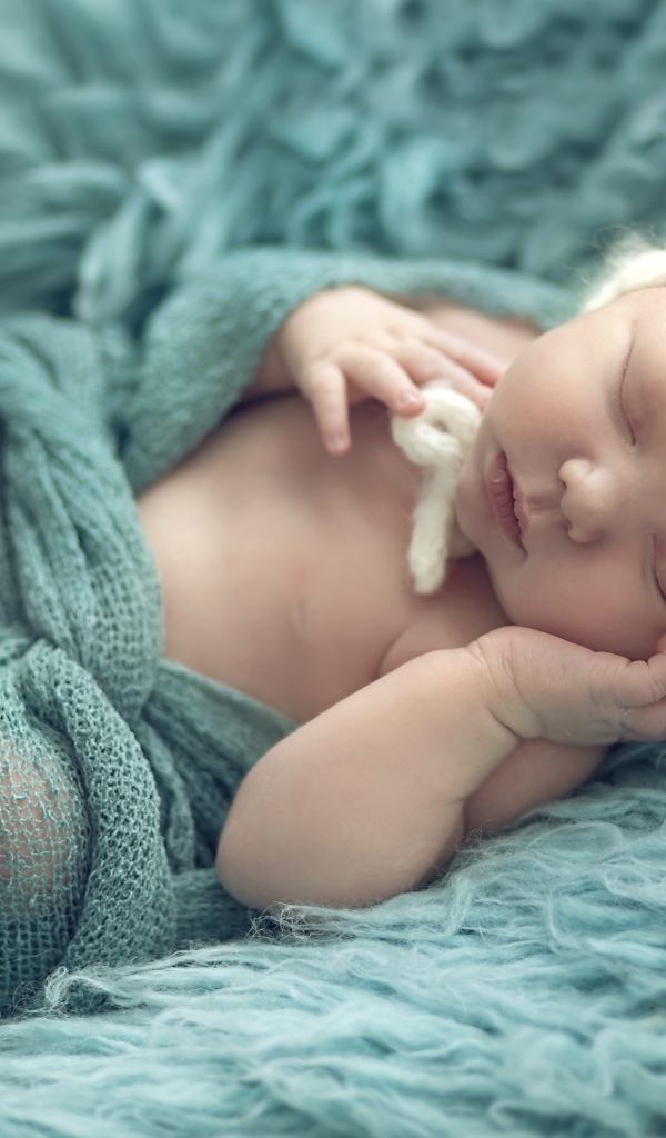 Грудной ребенок спит на зеленом меховом покрывале