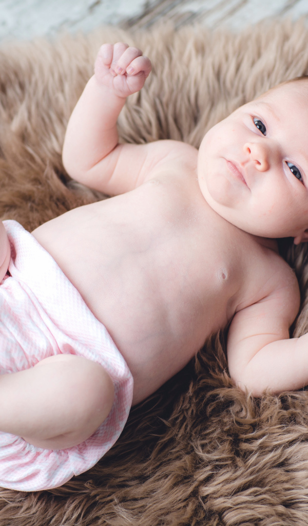 Грудной ребенок лежит на меховом покрывале