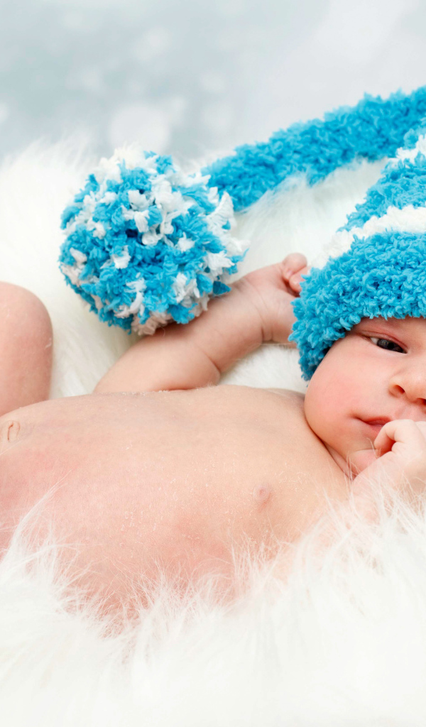 Грудной ребенок в голубой шапке с бубоном на голове