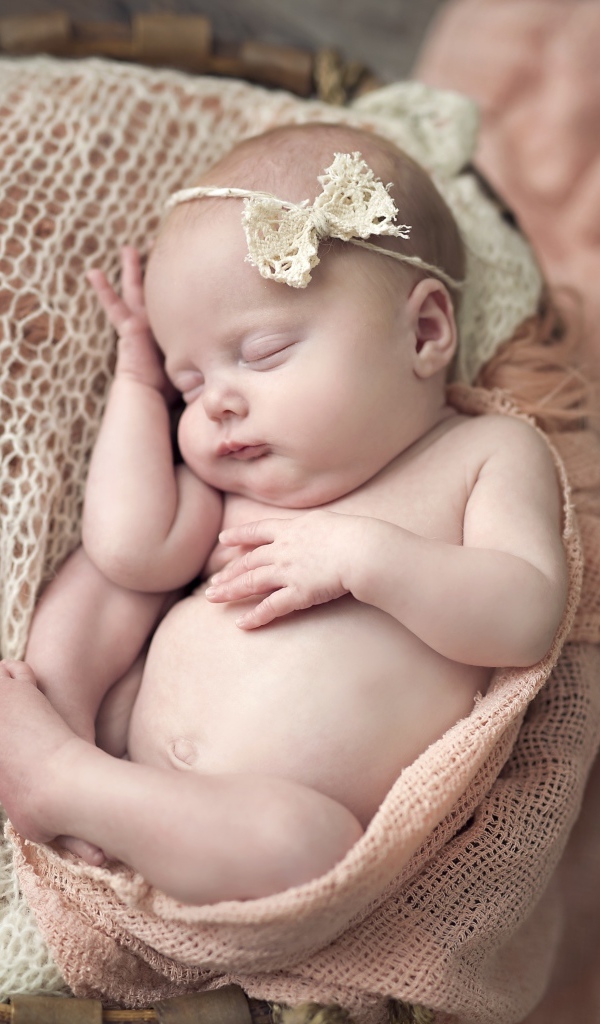 Грудной ребенок с бантиком на голове спит в корзине