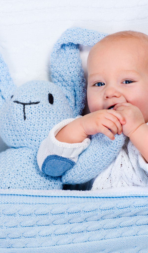 Милый младенец лежит в кроватке с голубым вязаным зайцем