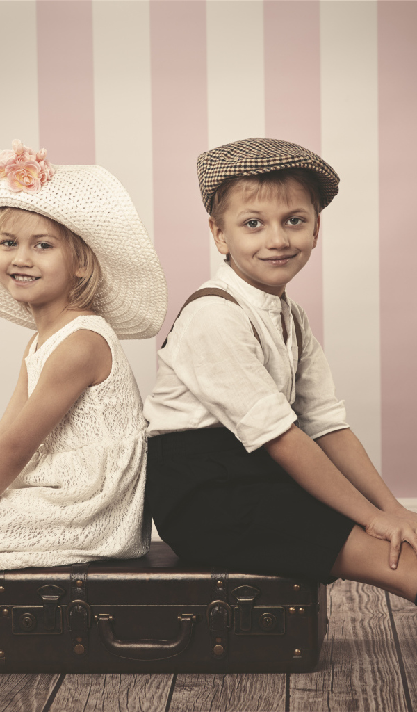 Девочка в большой белой шляпе и мальчик сидят на чемодане