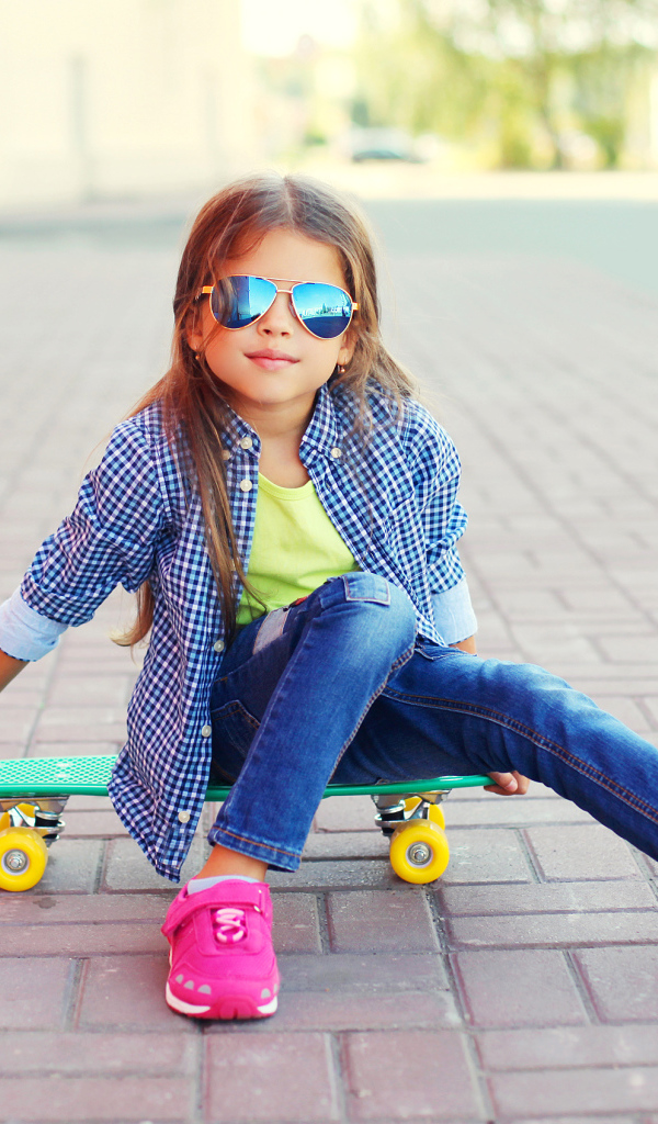 Девочка в солнечных очках сидит на скейтборде