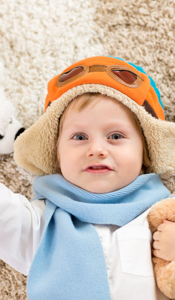 Маленький мальчик в шапке и игрушечным самолетом и медвежонком в руках