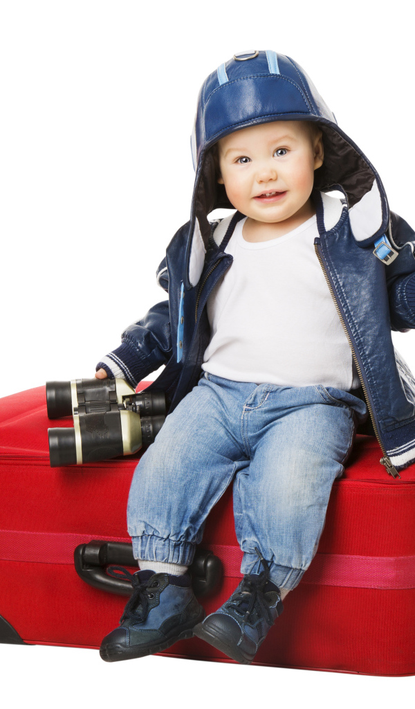 Маленький мальчик в шапке с биноклем сидит на красном чемодане