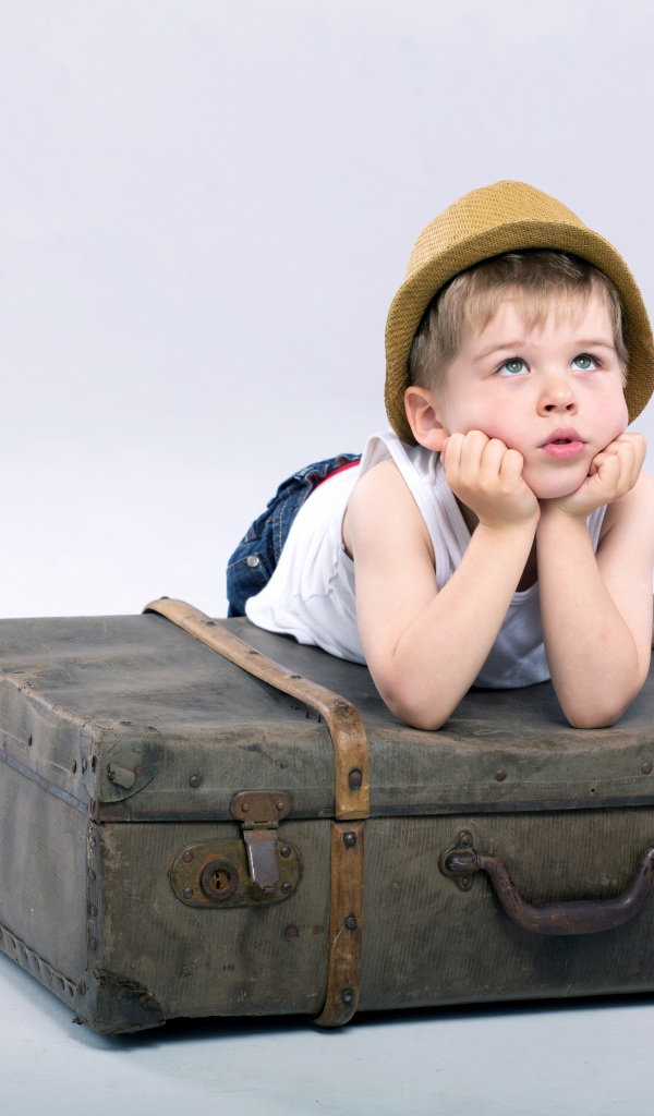 Маленький мальчик лежит на большом чемодане на сером фоне