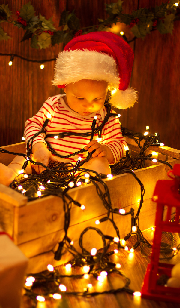 Маленький мальчик сидит в коробке с новогодней гирляндой