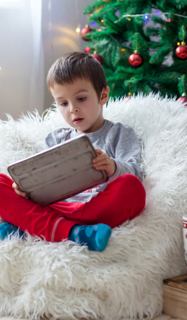 Маленький мальчик сидит в мягком кресле у новогодней елки