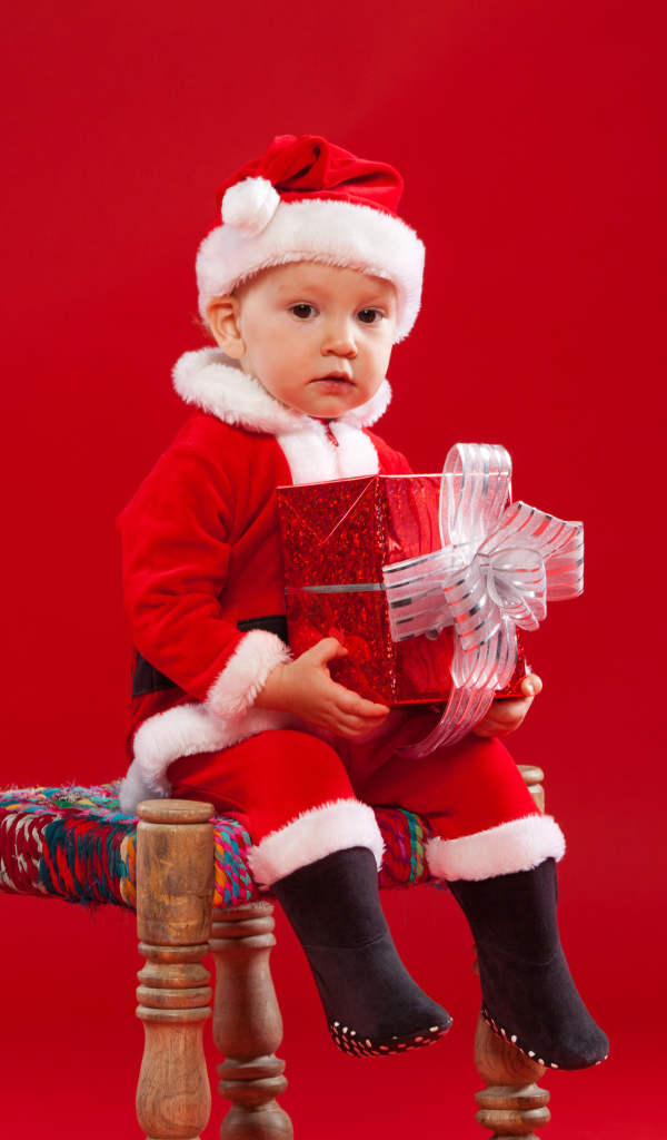 Маленький мальчик сидит на стуле с новогодним подарком