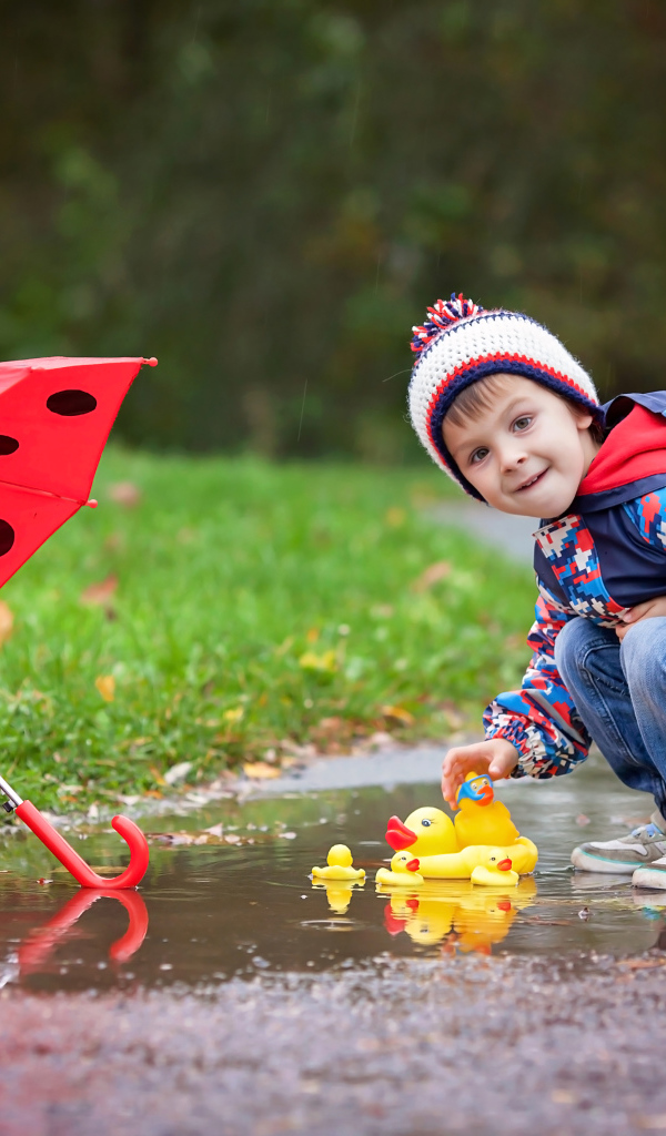 Маленький мальчик пускает резиновую уточку в лужу после дождя