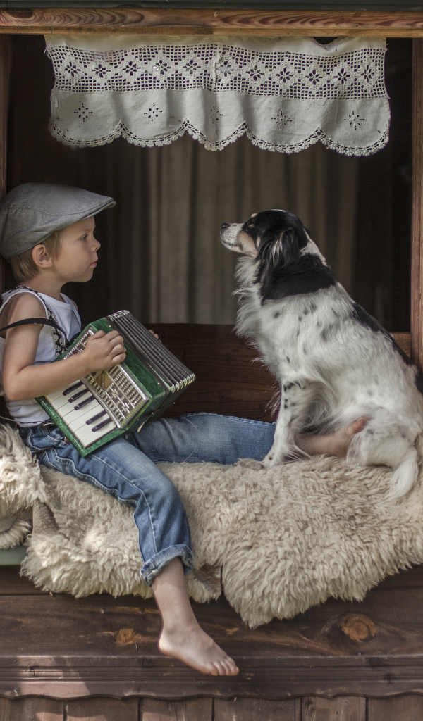 Маленький мальчик с гармошкой сидит на подоконнике с собакой