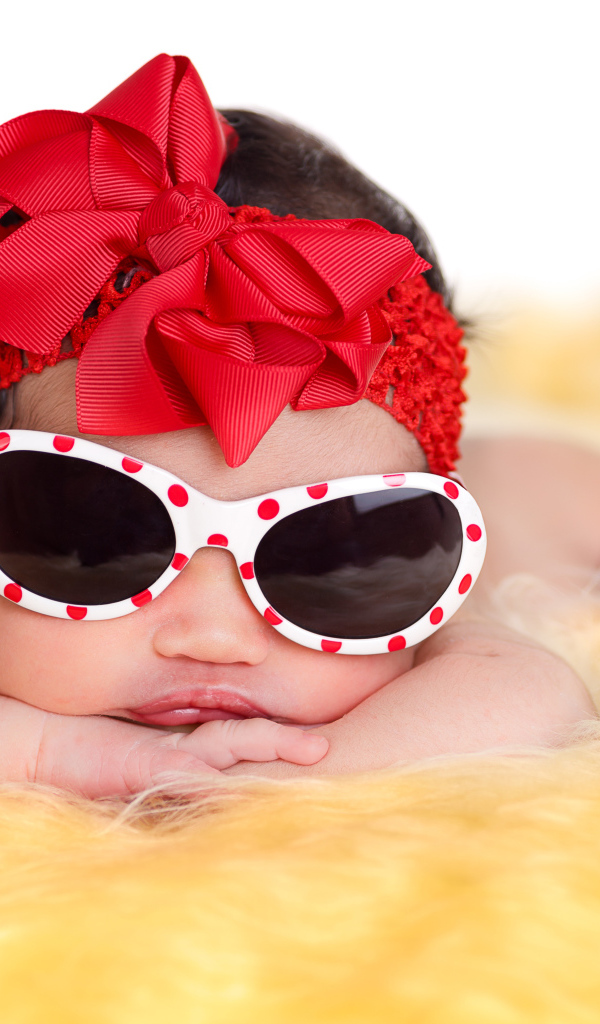 Маленькая забавная малышка в очках и с красным бантом на голове