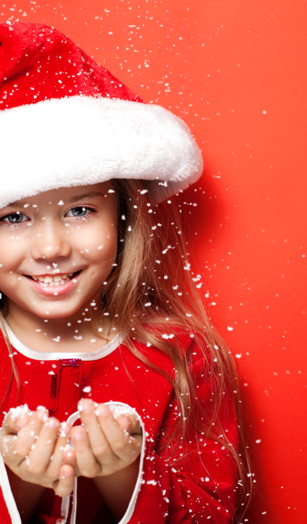 Маленькая девочка в новогодней шапке ловит руками снежинки