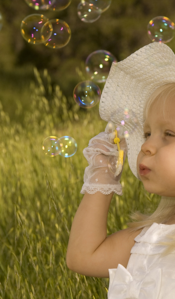 Маленькая девочка в большой белой шляпе пускает мыльные пузыри
