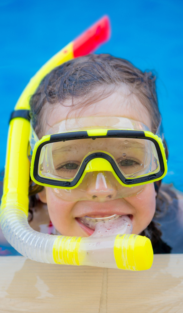 Маленькая девочка в маске с трубкой плавает в бассейне