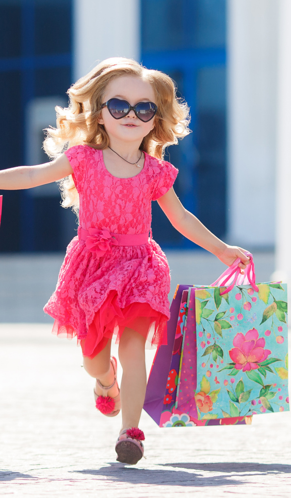 Маленькая девочка в розовом платье бежит с покупками из магазина