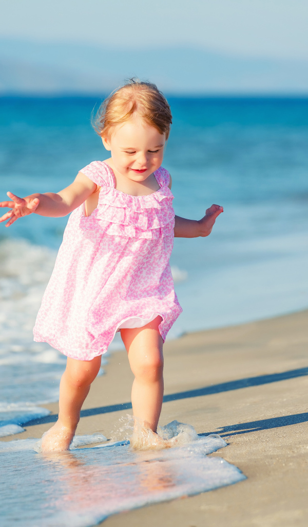 Маленькая девочка в розовом платье гуляет по морскому песку