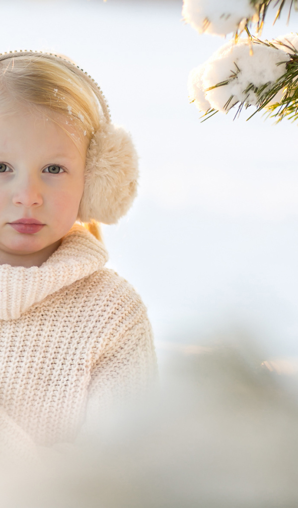 Маленькая девочка в белом свитере у покрытой снегом ели
