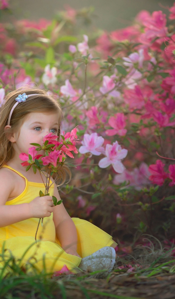 Маленькая девочка в желтом платье сидит рядом с розовыми цветами