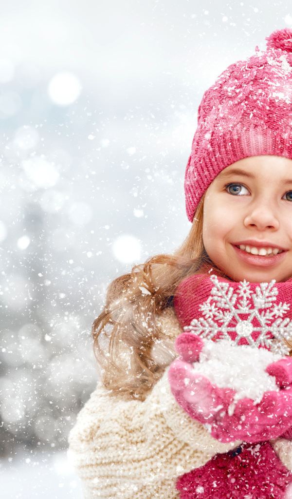 Маленькая девочка в зимней одежде держит снег в руках