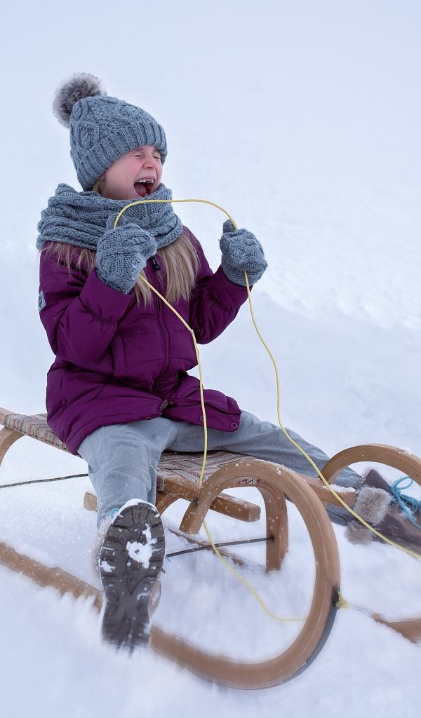 Маленькая девочка едет на санях с горки зимой