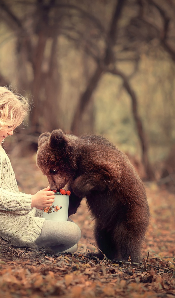 Маленькая девочка сидит у дерева с медвежонком гризли