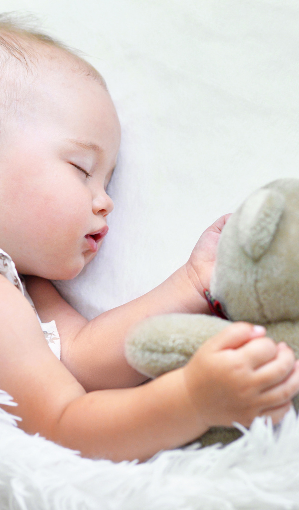 Маленькая девочка спит с мягкой игрушкой под белым одеялом