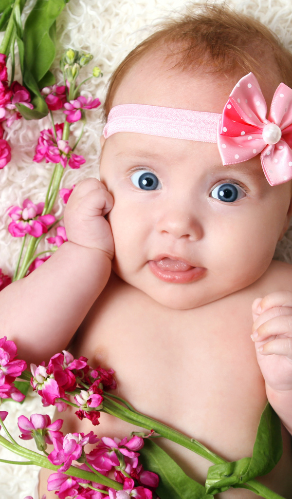 Маленькая девочка с бантиком на голове лежит с цветами левкой