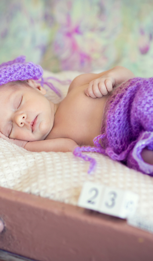 Маленький спящий младенец в вязаном фиолетовом костюме