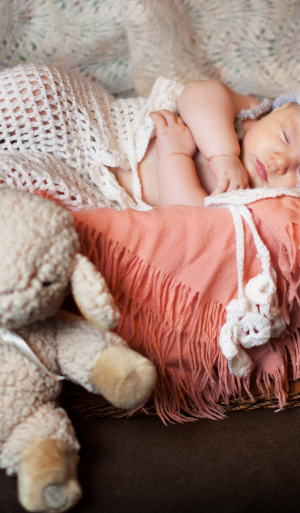 Спящий грудной ребенок в забавной шапке с мягкой игрушкой