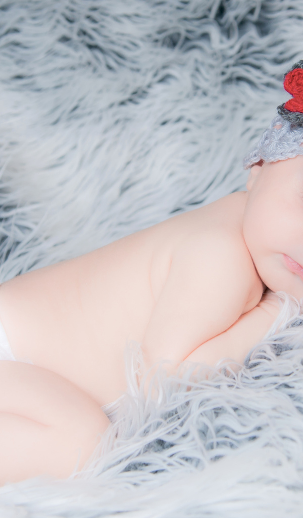 Спящий грудной ребенок в вязаной шапке с красным цветком на голове