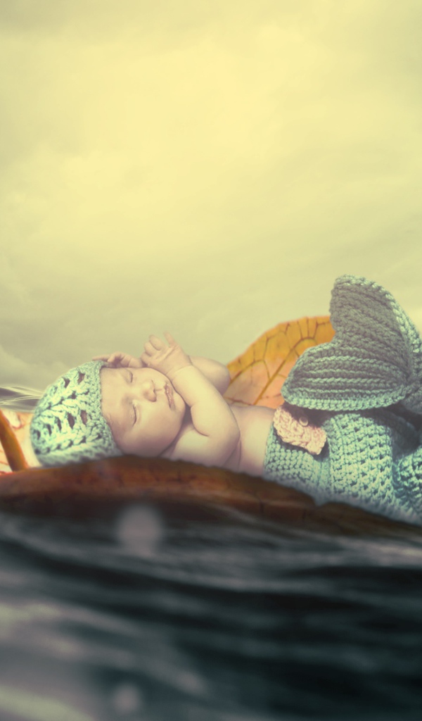 Маленький грудной ребенок в костюме русалки плывет на листе в океане