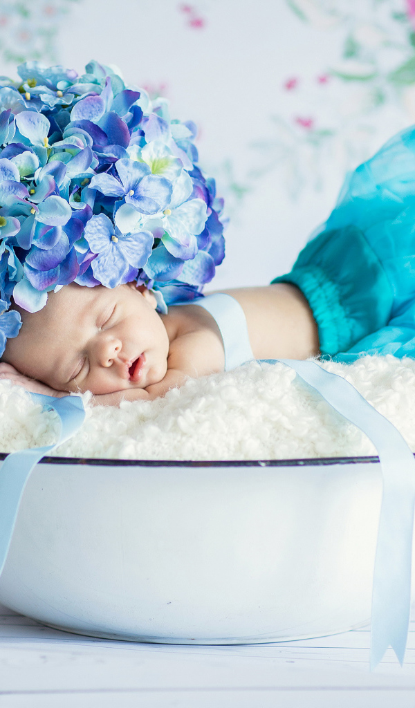 Маленький грудной ребенок спит в миске с шапкой из цветов гортензии на голове