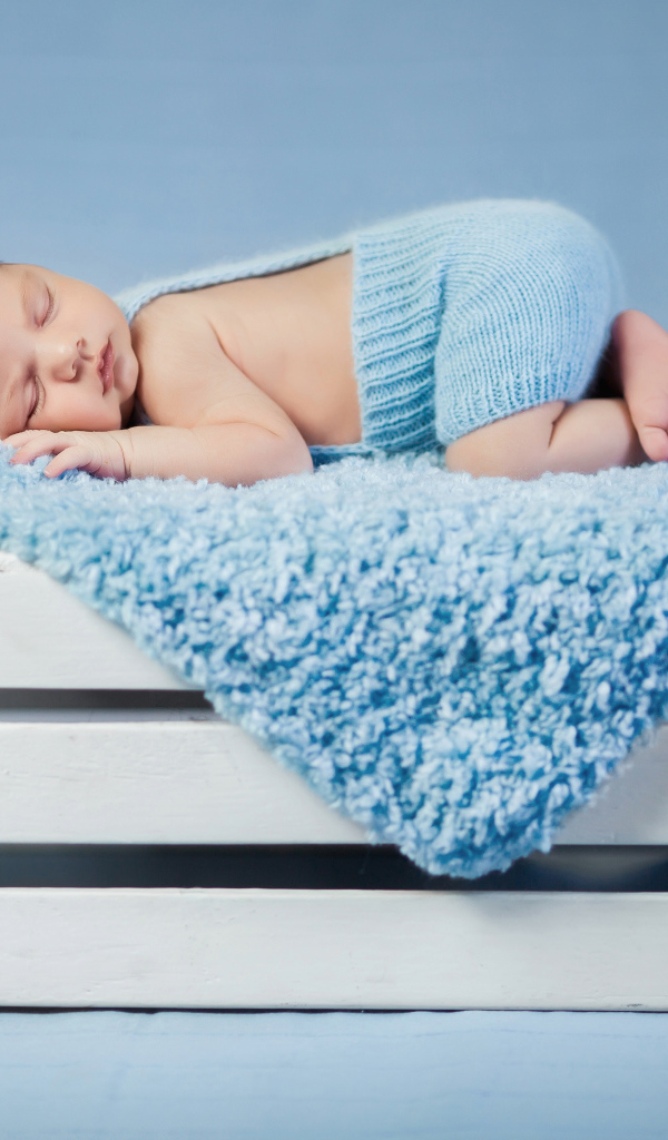 Маленький грудной ребенок спит на синем покрывале на деревянном ящике