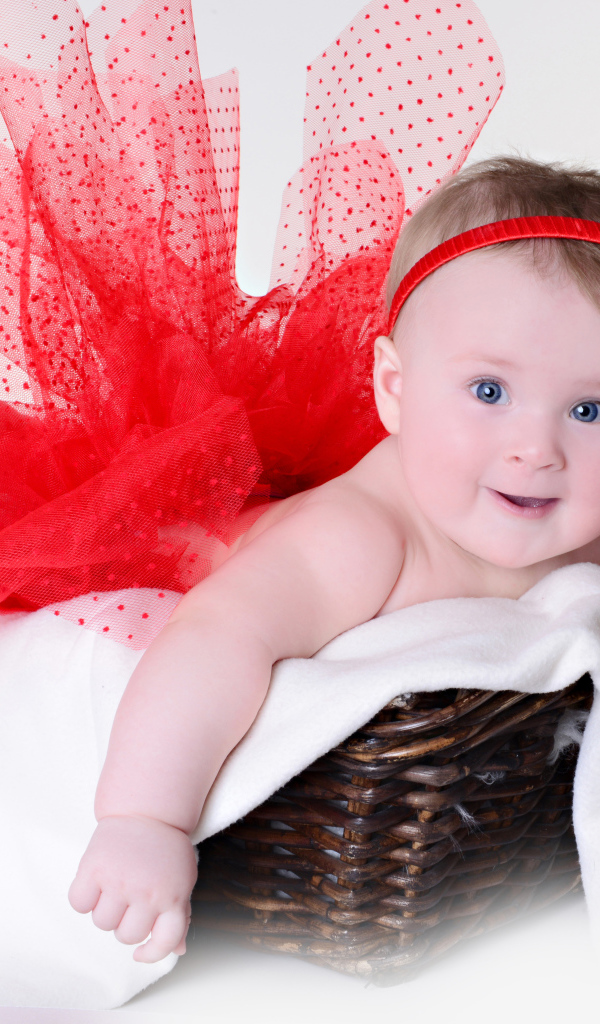 Маленькая голубоглазая девочка в красном красивом платье лежит в корзине