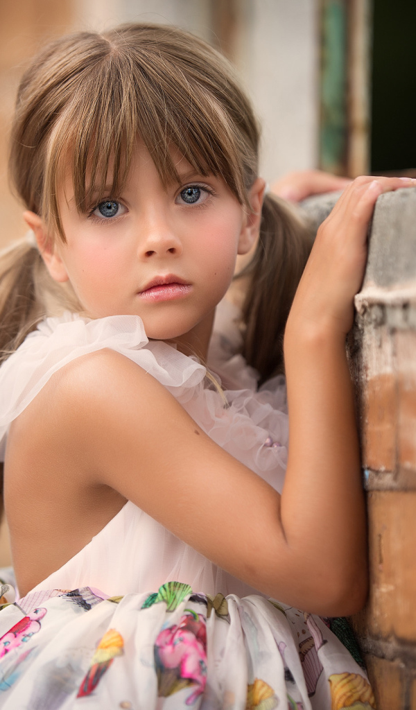 Милая девочка с серьезным взглядом стоит у стены