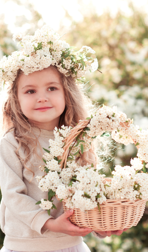 Милая маленькая девочка с венком на голове и корзиной белых цветов