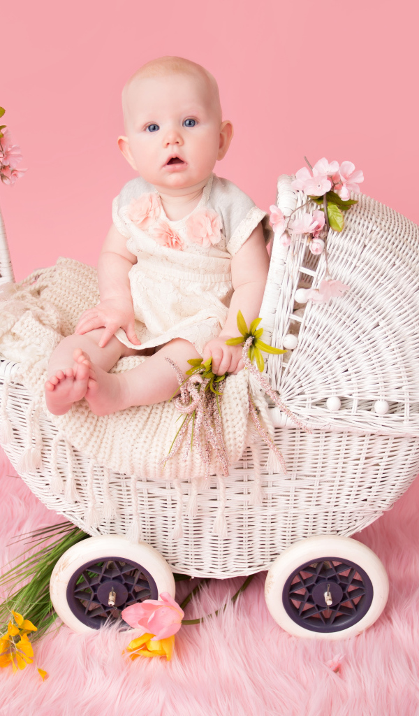 Младенец девочка сидит в коляске на розовом фоне