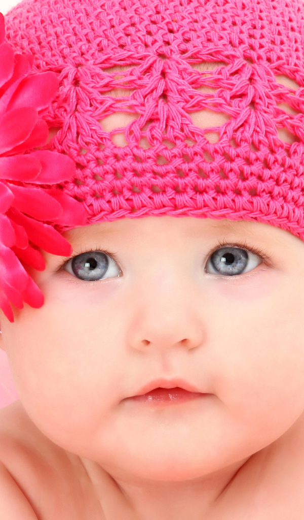 Милая голубоглазая малышка в розовой шапке с цветком герберы