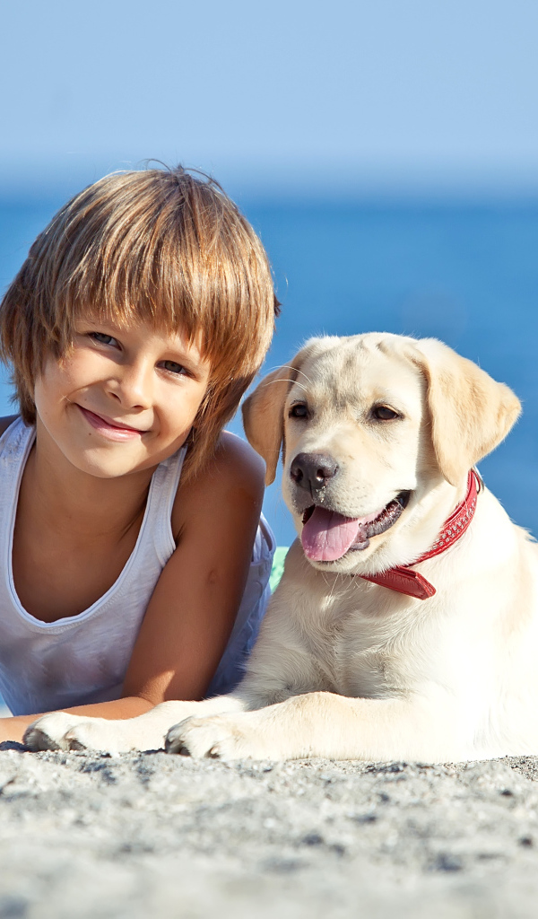 Симпатичный мальчик со щенком ретривера лежат на песке на пляже