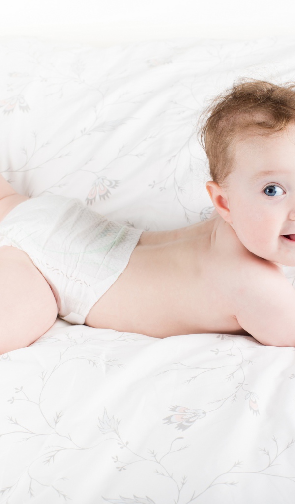 Забавный голубоглазый малыш лежит на белом покрывале