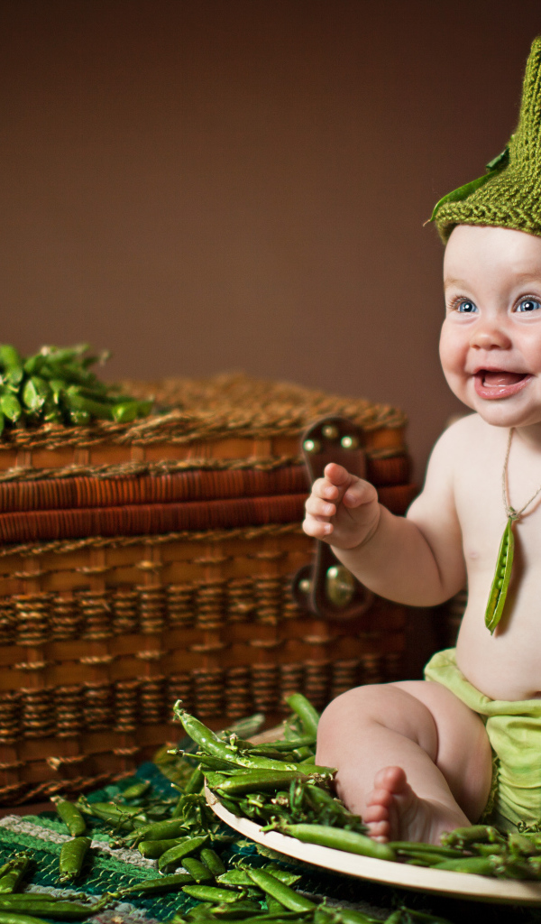 Забавный улыбающийся малыш сидит на стручках зеленого гороха