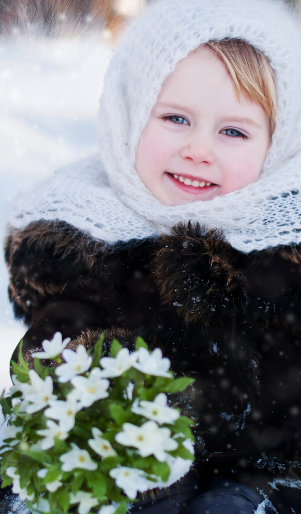 Маленькая голубоглазая девочка с букетом подснежников зимой