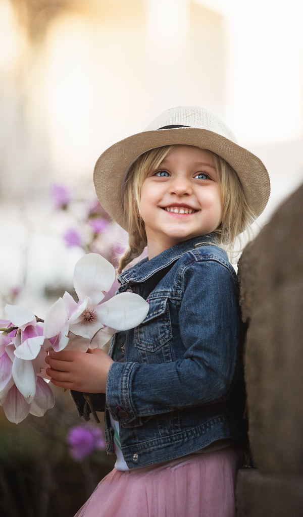Маленькая голубоглазая улыбающаяся девочка в шляпе с букетом в руках