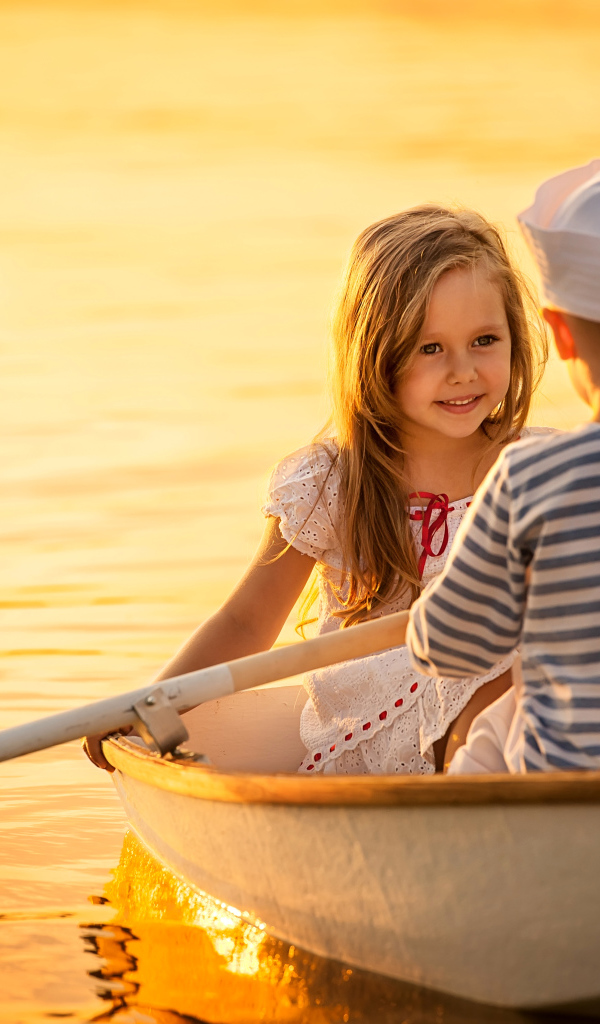 Маленькие мальчик и девочка плывут в лодке на закате солнца