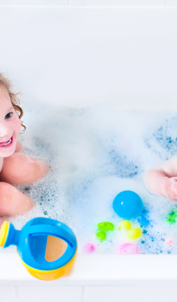 Маленькие мальчик и девочка купаются в ванной с игрушками