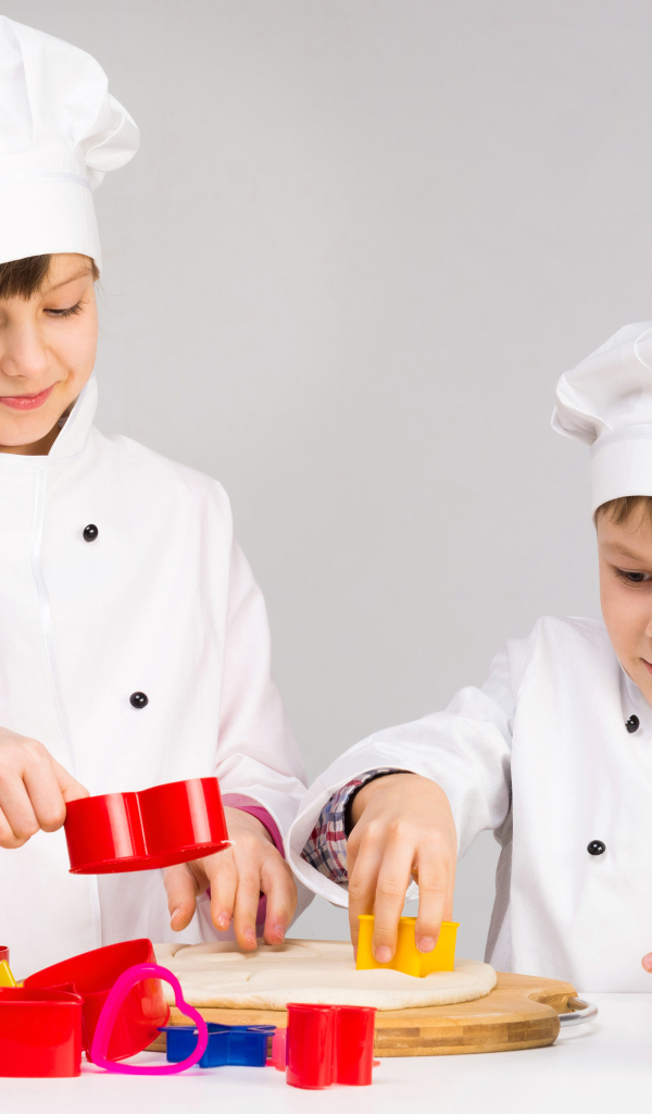 Маленькие мальчик и девочка готовят на кухне печенье