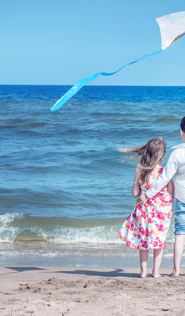 Маленькие мальчик и девочка запускаю воздушного змея на пляже